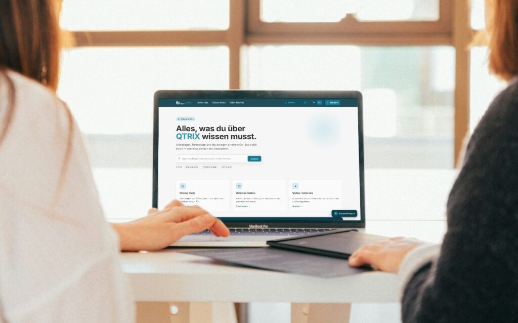 Zwei Kolleginnen in einer Besprechung, auf dem Laptop die Startseite der QTRIX-Hilfe